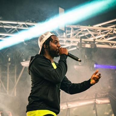 capo lee holds a microphone on stage and wears a cap backwards