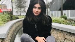 person sitting on a low wall in a black hoody, brick walls visible behind them