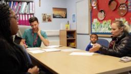 four people sitting around a table talking in a school classroom