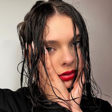 a woman with wet brown hair holds her hands against her cheeks