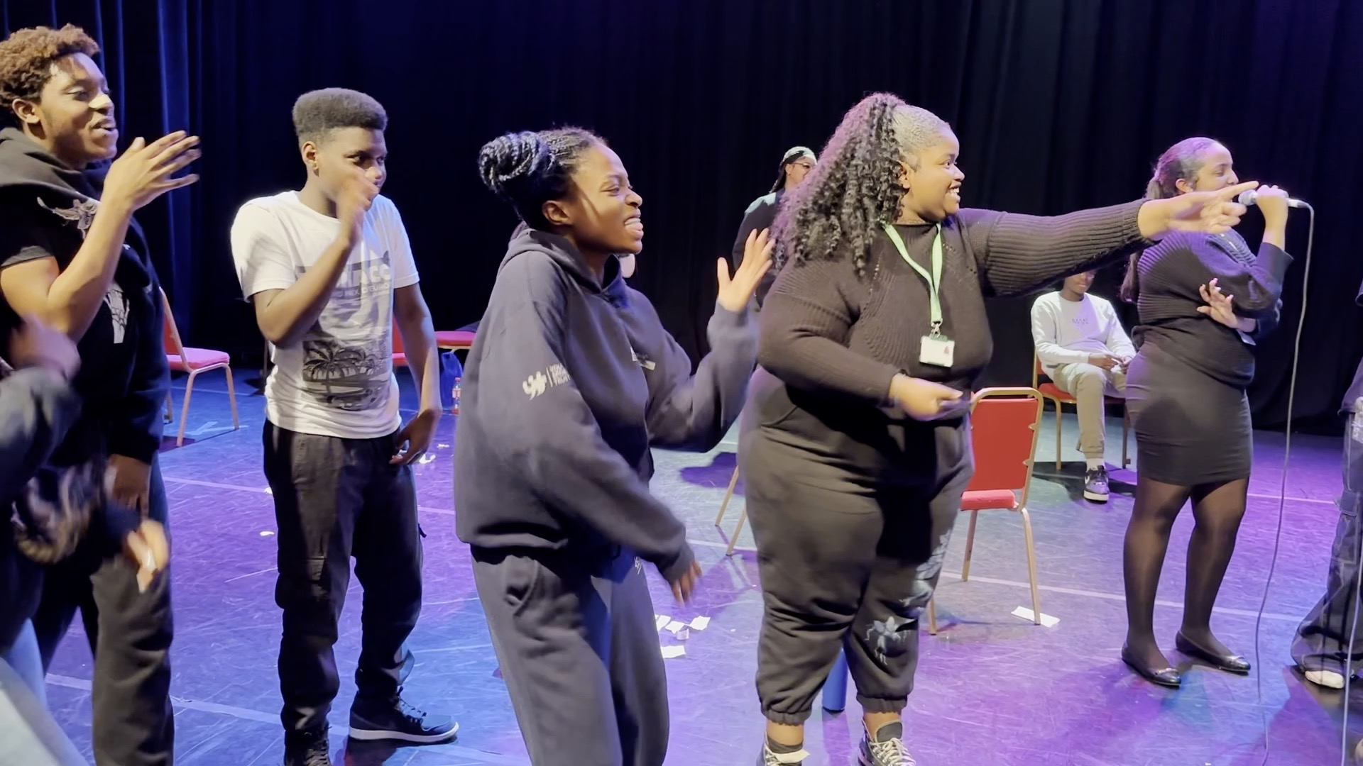 a group of young people stand spread out on stage; they are involved in an activity