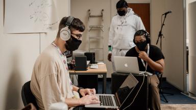 three people in a room wearing face masks working on laptops