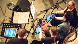 Group of people making music on tablets wearing Drake Music t-shirts