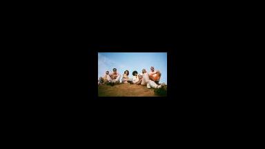 seven people sitting on grassy hill with blue sky in background