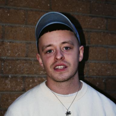 luke rv wears a white t shirt, silver necklace and denim cap.