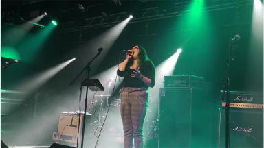 woman singing into microphone on a stage, under green lights