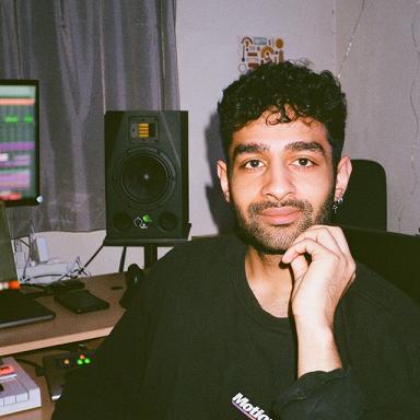 michael diamond faces the camera. he wears a long-sleeve black t-shirt and has dark hair and stubble around his chin. computer equipment is in the background.