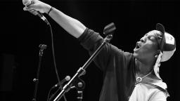 black and white photo of young person on stage pointing a microphone into the air