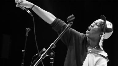 black and white photo of young person on stage pointing a microphone into the air