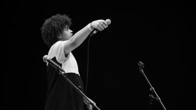 young man with an afro holds a microphone out