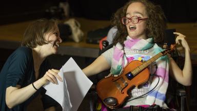 Young musician playing an adapted violin with adult holding up sheet music for them