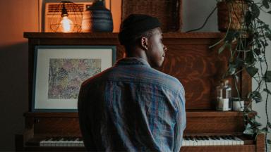 person with their back to the camera, sitting at a piano, looking out the window