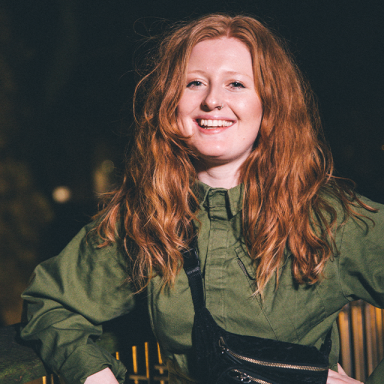 a woman with red hair smiles and wears a khaki dress