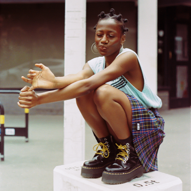 bina wears her hair in bantu knots and crouches on a white box.