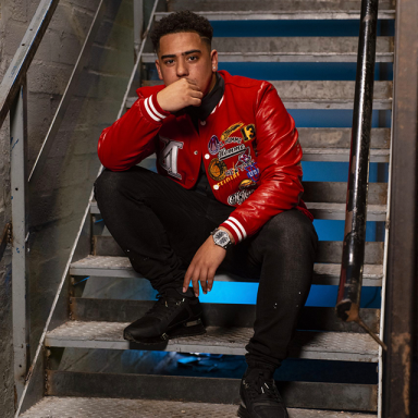 a man wears a red jacket and black trousers and sits on the stairs