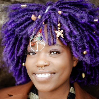 a woman smiles, her hair is purple and she wears charms in it