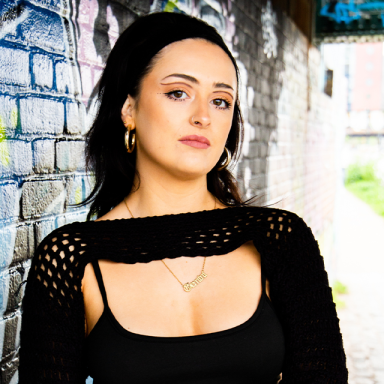 freya wears a black top and poses against a brick wall