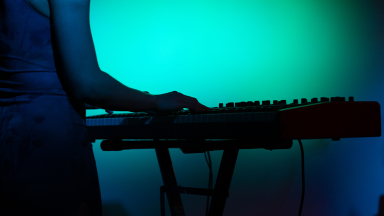 a woman plays an electronic instrument. the room is illuminated in a turquoise hue