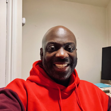 a man wears a red hoodie and smiles