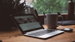 photo of an open macbook and mug on a wooden desk in front of a window