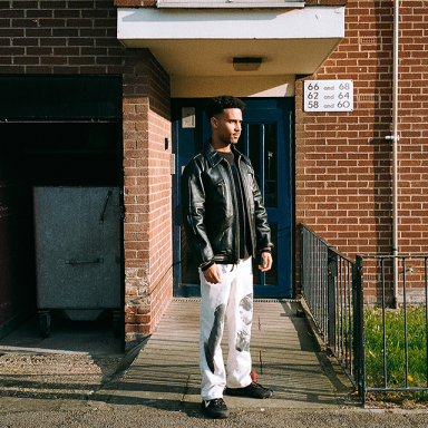 a person wears a black leather jacket and stands outside a brick building